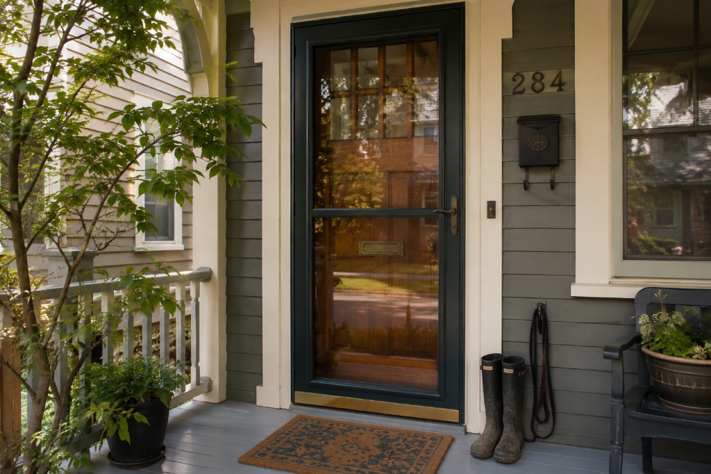 Green storm door on a sage-sided craftsman front porch